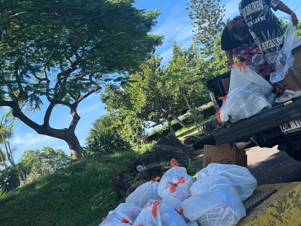 Volunteers unloading bagged food from a pickup truck at a community food distribution in Kona.