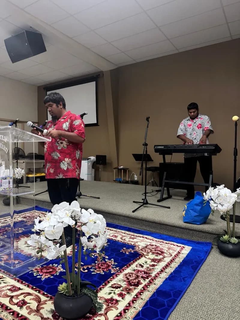 A Sunday service in progress, with the preacher at a clear pulpit and a keyboard player leading music behind him.
