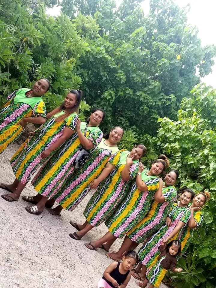 Women of the church lined up in bright patterned dresses under the trees at an outdoor gathering.